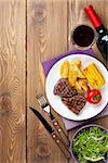 Steak with grilled potato, corn, salad and red wine over wooden table. Top view with copy space