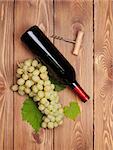 Red wine bottle and bunch of white grapes on wooden table background