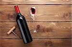 Red wine bottle, glass of wine and corkscrew. View from above over rustic wooden table background with copy space