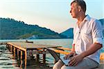 man in a white shirt with a laptop on the pier to meet a dawn