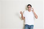 Portrait of handsome Indian guy enjoying music, standing on plain background with shadow, looking at camera.