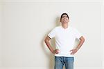 Portrait of handsome Indian guy looking up, standing on plain background with shadow, copy space at side.