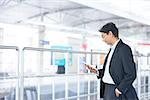 Asian Indian businessman using tablet pc while waiting train at railway station.