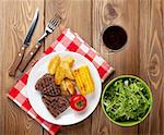 Steak with grilled potato, corn, salad and red wine on wooden table