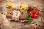 Two sandwiches with salad, ham, cheese and tomatoes on wooden table. Top view