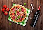 Italian pizza with pepperoni and red wine on wooden table. Top view