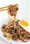 Close-up stir fried char kuey teow on chopstick over wooden background.