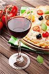 Glass of red wine and italian pizza with cheese, tomatoes, olives and basil