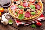 Italian pizza with pepperoni, tomatoes, olives, basil and red wine on wooden table. Top view