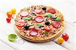 Italian pizza with pepperoni, tomatoes, olives and basil on wooden table