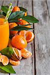 Glass of fresh tangerine juice with ripe tangerines, leaves and old-fashioned straws. Copy space background.