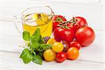 Fresh colorful tomatoes, basil and olive oil on white wooden table