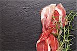 Prosciutto with rosemary on black stone table