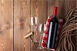 Red wine bottle, glasses and corkscrew over rustic wooden table background with copy space