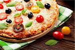 Italian pizza with cheese, tomatoes, olives and basil on wooden table