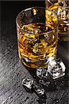 Glasses of whiskey with ice on black stone table