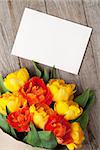 Colorful tulips bouquet and blank greeting card over wooden table background with copy space