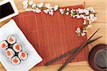 Sushi maki set, green tea and sakura branch over bamboo table with copy space