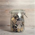 Coins in glass money jar, financial concept. Vintage wooden background with dramatic light.