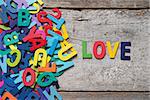 The colorful words "LOVE" made with wooden letters next to a pile of other letters over old wooden board.