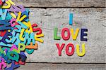 The colorful words "I LOVE YOU" made with wooden letters next to a pile of other letters over old wooden board.