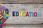 The colorful words "EDUCATION" made with wooden letters next to a pile of other letters over old wooden board.