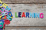 The colorful words "LEARNING" made with wooden letters next to a pile of other letters over old wooden board.