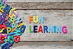 The colorful words "FUN LEANRING" made with wooden letters next to a pile of other letters over old wooden board.