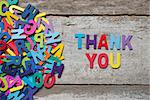 The colorful words "THANK YOU" made with wooden letters next to a pile of other letters over old wooden board.