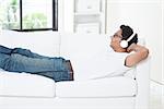 Indian guy enjoying music at home. Asian man with headset listening to song, relaxed and lying on sofa indoor. Handsome male model.