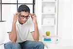 Indian guy having headache at home. Asian man hands holding head sitting on sofa indoor. Handsome male portrait.