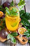 Homemade lemonade with passionfruit, mint leaves and ice cubes on old wooden background