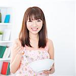 Happy Asian housewife with apron preparing food, using manual egg mixer and bowl. Young woman indoors living lifestyle at home.