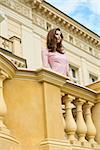 fashion outside shoot of very pretty woman with elegant pink dress and long natural hair posing on balcony of ancient palace