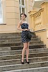 fashion  outside portrait of happy stylish girl with elegant hair-style, short dress and hat in the hand posing on staircase of old building