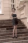 black and white fashion  outside portrait of happy stylish girl with elegant hair-style, short dress and hat in the hand posing on staircase of old building