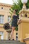 elegant brunette model posing in outside fashion shoot with sexy short dress, heels and stylish hat in the hand. Posing on staircase of old building