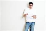 Portrait of handsome Indian guy using tablet pc, standing on plain background with shadow, copy space at side.