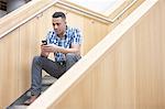 Young businessman sitting on office stairway texting on smartphone