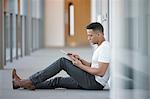 Young businessman sitting in office corridor using digital tablet