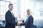 Portrait of young businesswoman shaking hands with businessman in office