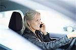 Mature businesswoman chatting on smartphone whilst driving car