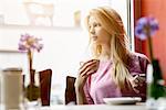 Young woman gazing out of cafe window whilst drinking coffee