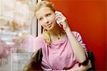 Young woman gazing out of cafe window whilst chatting on smartphone