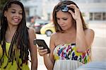 Two young female friends reading texts on smartphone, Copacabana, Rio De Janeiro, Brazil