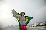 Smiling young man holding up Brazilian flag on Ipanema beach, Rio De Janeiro, Brazil