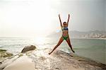 Young woman wearing bikini jumping mid air on  Ipanema beach, Rio De Janeiro, Brazil
