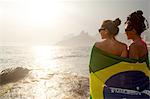 Rear view of  two young women wrapped in Brazilian flag, Ipanema beach, Rio De Janeiro, Brazil