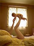 Mother lying on bed balancing baby son on feet