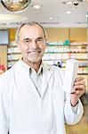 Portrait of senior male pharmacist holding up medicine in pharmacy